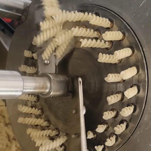 R.N. fusilli die mounted on an extruder with spiral pasta emerging from rings of openings